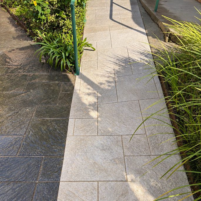 Stamped concrete path half cleaned, showing the clean side next to the dark slippery side
